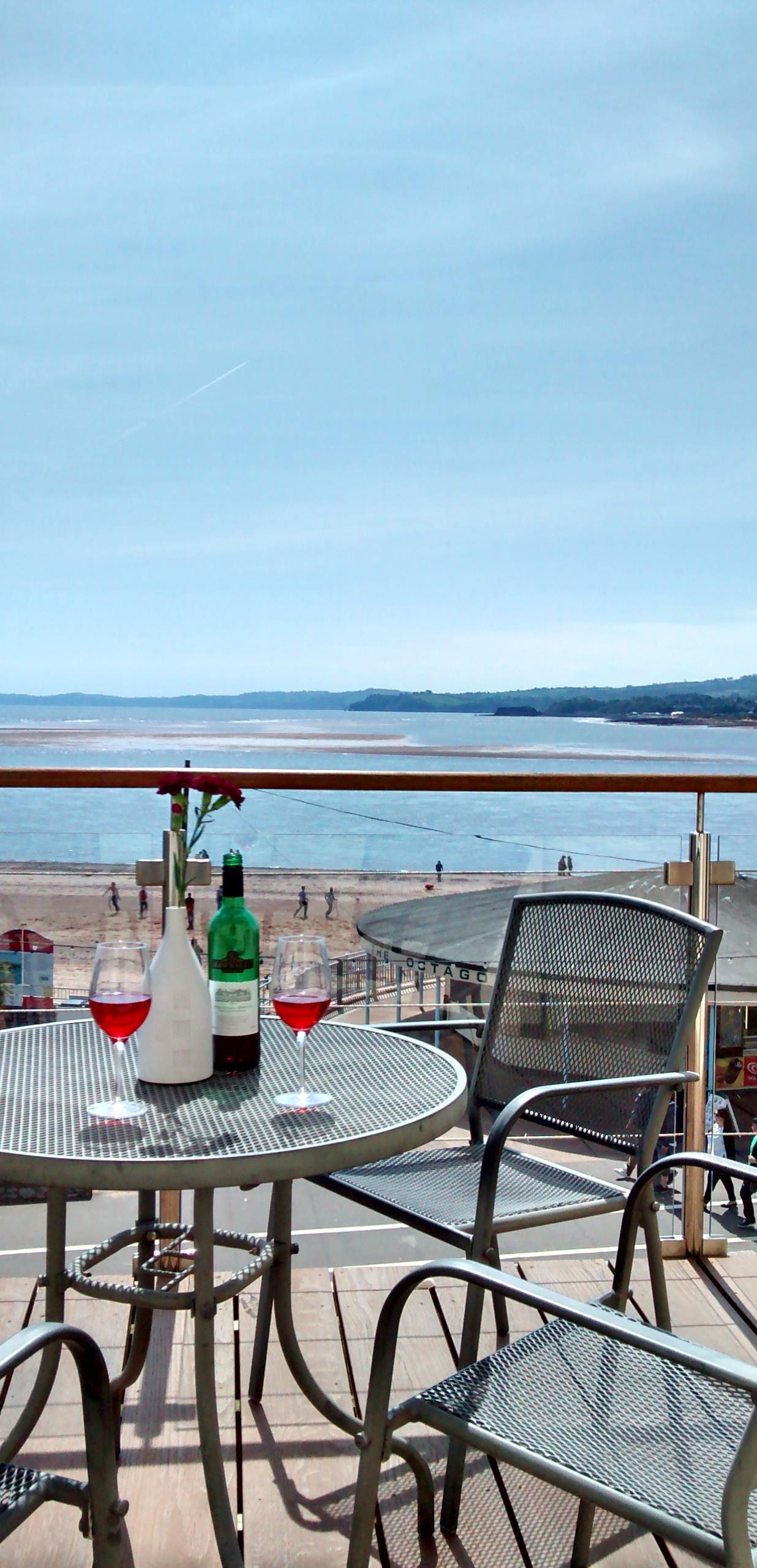 View across balcony table with wine bottle out to sea